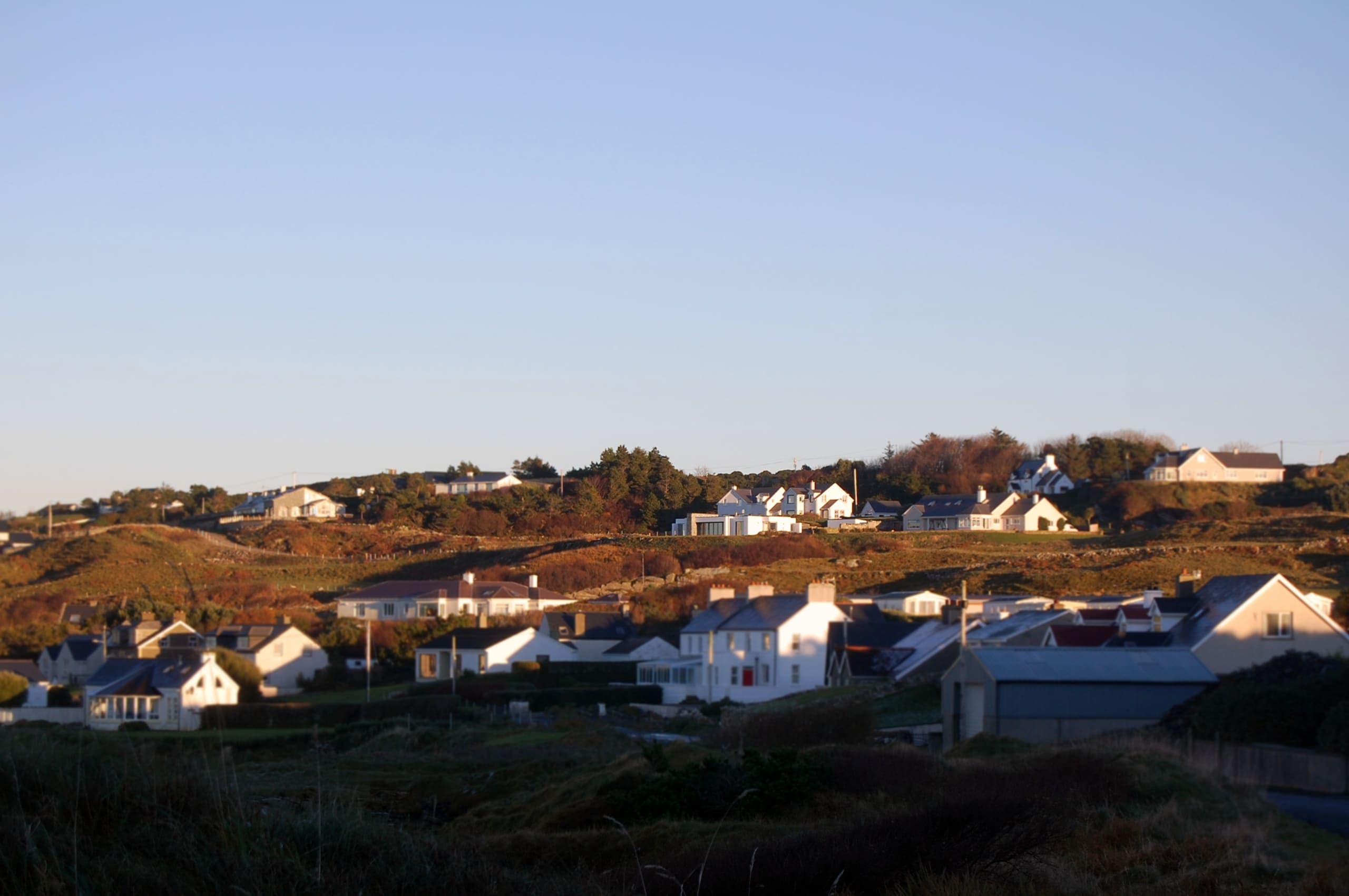 White houses on a Donegal hillside in low evening sun, under a clear sky